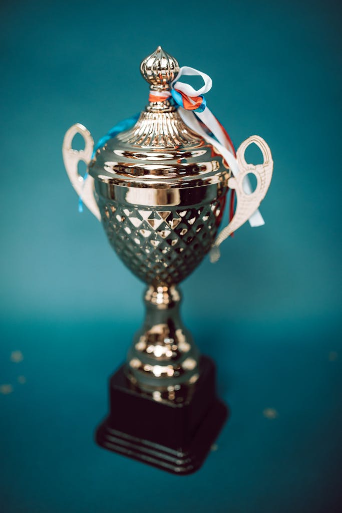 Close-up of a shiny silver trophy adorned with ribbons, set against a blue background.