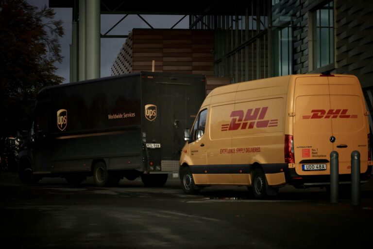 DHL and UPS delivery trucks parked at night near a modern building, ready for logistics operations.