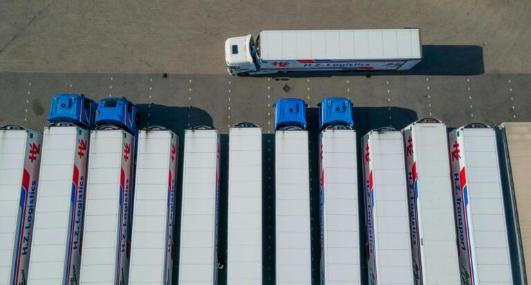 Top-down drone shot of logistics trucks arranged in a row in a parking lot.